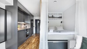 Ein gemütlicher Raum mit Bett, Küchenzeile und Blick auf einen Wald durch ein Fenster.