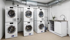 A laundry facility with four stacked washing machines, a sink, and a ventilation system.