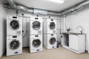 Une buanderie équipée de quatre machines à laver superposées, d’un évier et d’un système de ventilation.