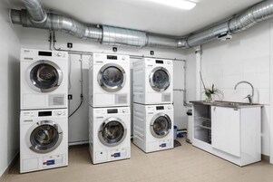 Una sala de lavandería con cuatro lavadoras apiladas, un lavabo y un sistema de ventilación.