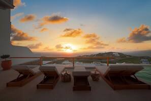 A sunset view from a balcony with lounge chairs and a potted plant.