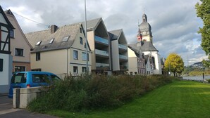 A multi-story building with a prominent clock tower, a blue van parked in front, and a well-maintained lawn. - Apartments Rheinblick-Koblenz (Neuendorf)
