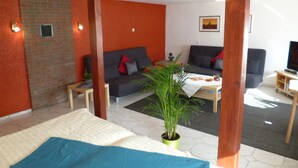 A modern living room with a sofa, a coffee table, and a TV. There is a brick wall and a wooden beam structure. - Apartments Rheinblick-Koblenz (Neuendorf)