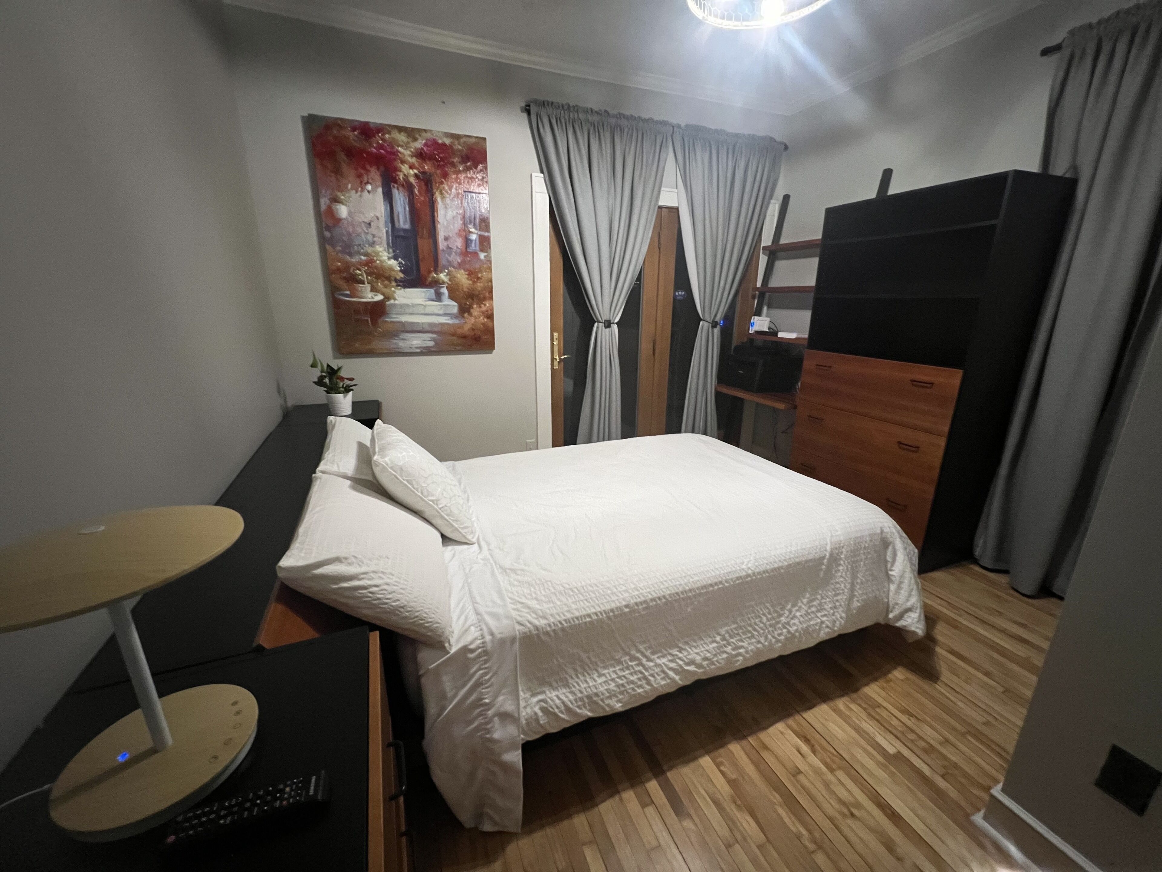 A bedroom with a bed, a desk, a dresser, and a painting on the wall.