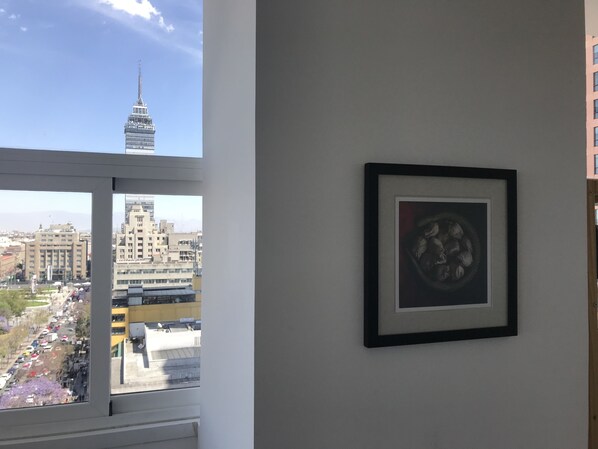 A room with a large window overlooking a cityscape, including a prominent tower. - LOFT MIRADOR / ALAMEDA CENTRAL / CDMX (Centro)