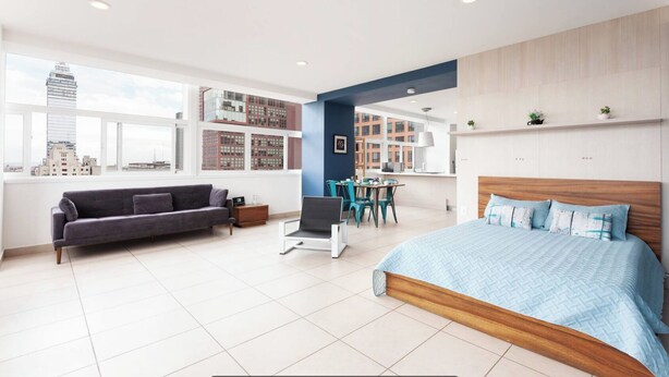 Ein modernes Hotelzimmer mit einem großen Bett, einer Couch, einem Schreibtisch und Blick auf die Stadt durch große Fenster.