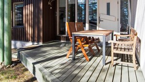 Une terrasse en bois avec une table et des chaises, une porte et de grandes fenêtres.