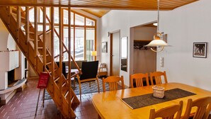 Un espace repas avec une table et des chaises en bois, un escalier et une vue sur l’extérieur.