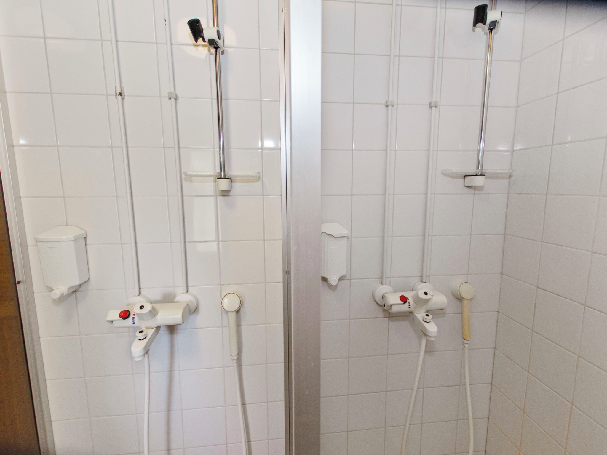 Une salle de bain avec des murs carrelés de carrelage blanc, des toilettes et une douche équipée d’un pommeau de douche à main et d’un flexible de douche.