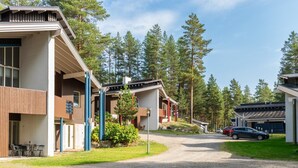 Un bâtiment moderne avec une allée de gravier menant à un espace de stationnement, le tout entouré de grands arbres.