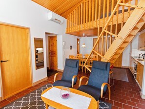 Un interior acogedor con una zona de comedor, dos sillas azules, una mesa con un vaso y una escalera de madera.