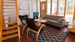 Un salon chaleureux avec une cheminée, un canapé, un téléviseur et une grande fenêtre donnant sur l’extérieur.