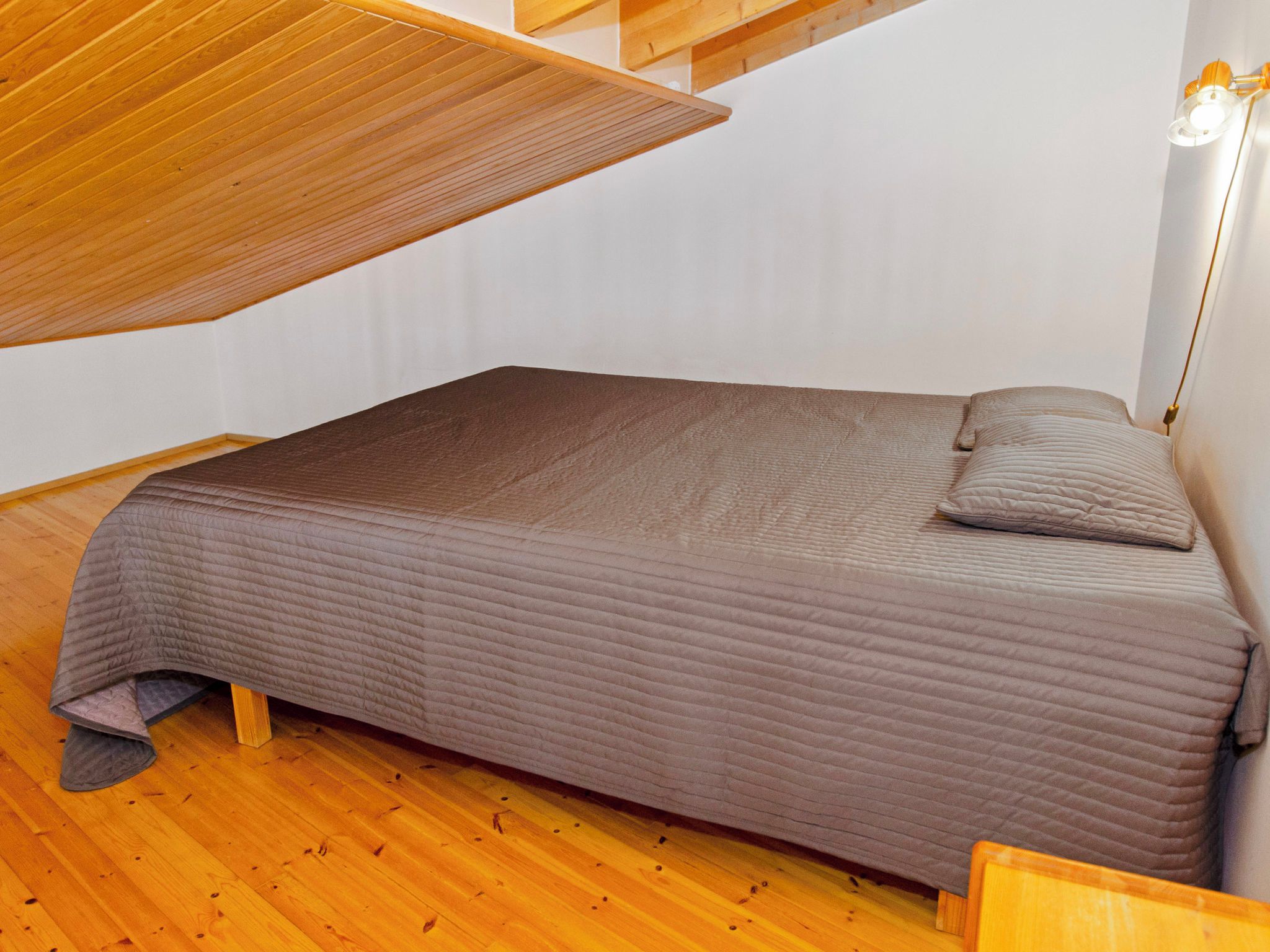 Een enkel bed met een gewatteerd matras en kussens in een kamer met houten vloer en een schuine plafond.