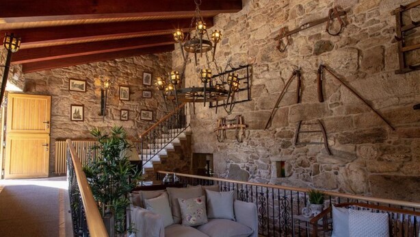 Un intérieur rustique avec un mur en pierre, un escalier en bois et un coin salon confortable avec un canapé et un banc.