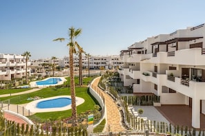 Un moderno resort con varias edificaciones blancas, una piscina central y palmeras.