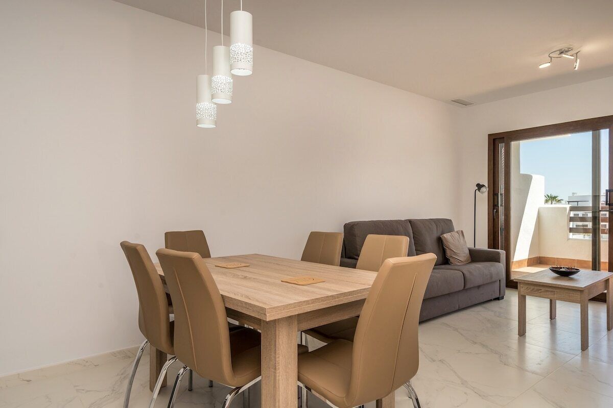 Un salon moderne avec un coin repas, comprenant une table et des chaises en bois, un canapé gris et une petite table d’appoint.