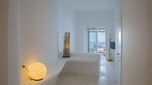A modern, minimalist hallway with a spherical light fixture, a sculptural piece, and a view into a room with a large window. - Villa Hermes (Mykonos)