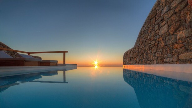 A serene infinity pool with a sunset view, stone walls, and a wooden deck with lounge chairs. - Villa Hermes (Mykonos)