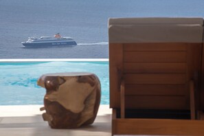A wooden lounge chair by a pool with a view of the ocean and a cruise ship in the distance. - Villa Hermes (Mykonos)
