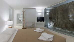 A modern hotel room with a large bed, a television, a stone wall aquarium, and a wooden chair. - Villa Hermes (Mykonos)