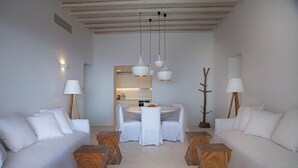 A modern, minimalist living room with white furniture, a round dining table, and wooden side tables. - Villa Hermes (Mykonos)