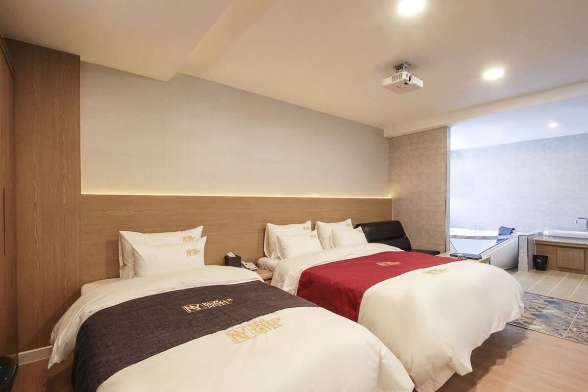 A hotel room with two beds, a desk, a chair, a window, and a bathroom.