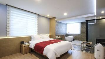 A modern hotel room with a large bed, a small bedside table, a nightstand, a bathroom with a bathtub, and a fireplace.