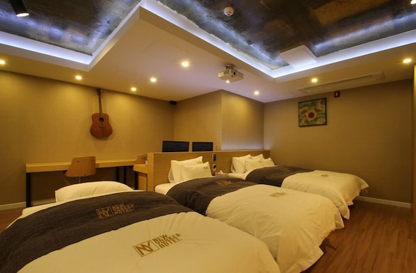 Una habitación de hotel con tres camas, una guitarra, un proyector y un cuadro en la pared.