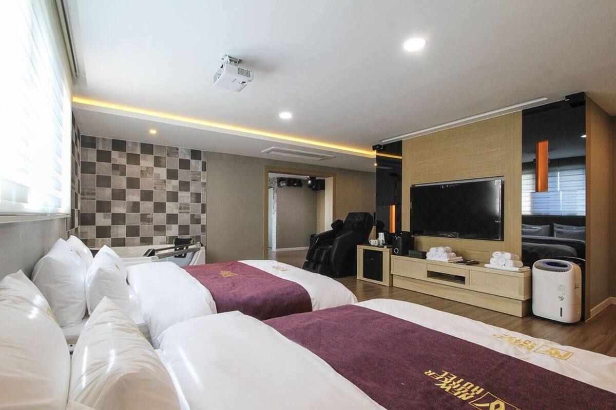 A hotel room with two beds, a television, a massage chair, and a minibar.