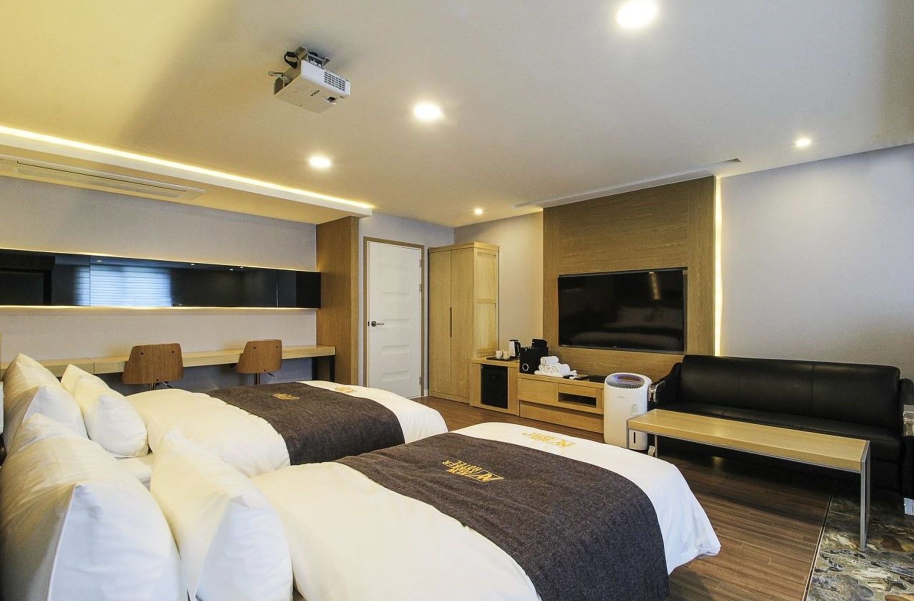 A modern hotel room with two beds, a flat-screen TV, a sofa, and a coffee machine.