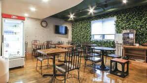 Ein Restaurant mit Holztischen und -stühlen, einem Kühlschrank, einem Fernseher und einer Wand mit grüner Bepflanzung.