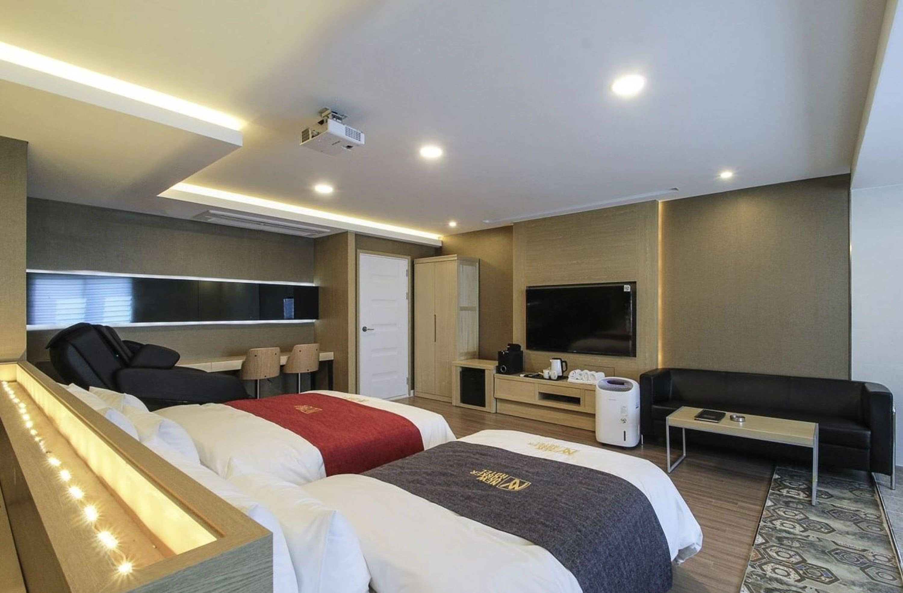 Una habitación de hotel moderna con dos camas, televisión, sofá, cafetera y un ventanal grande.
