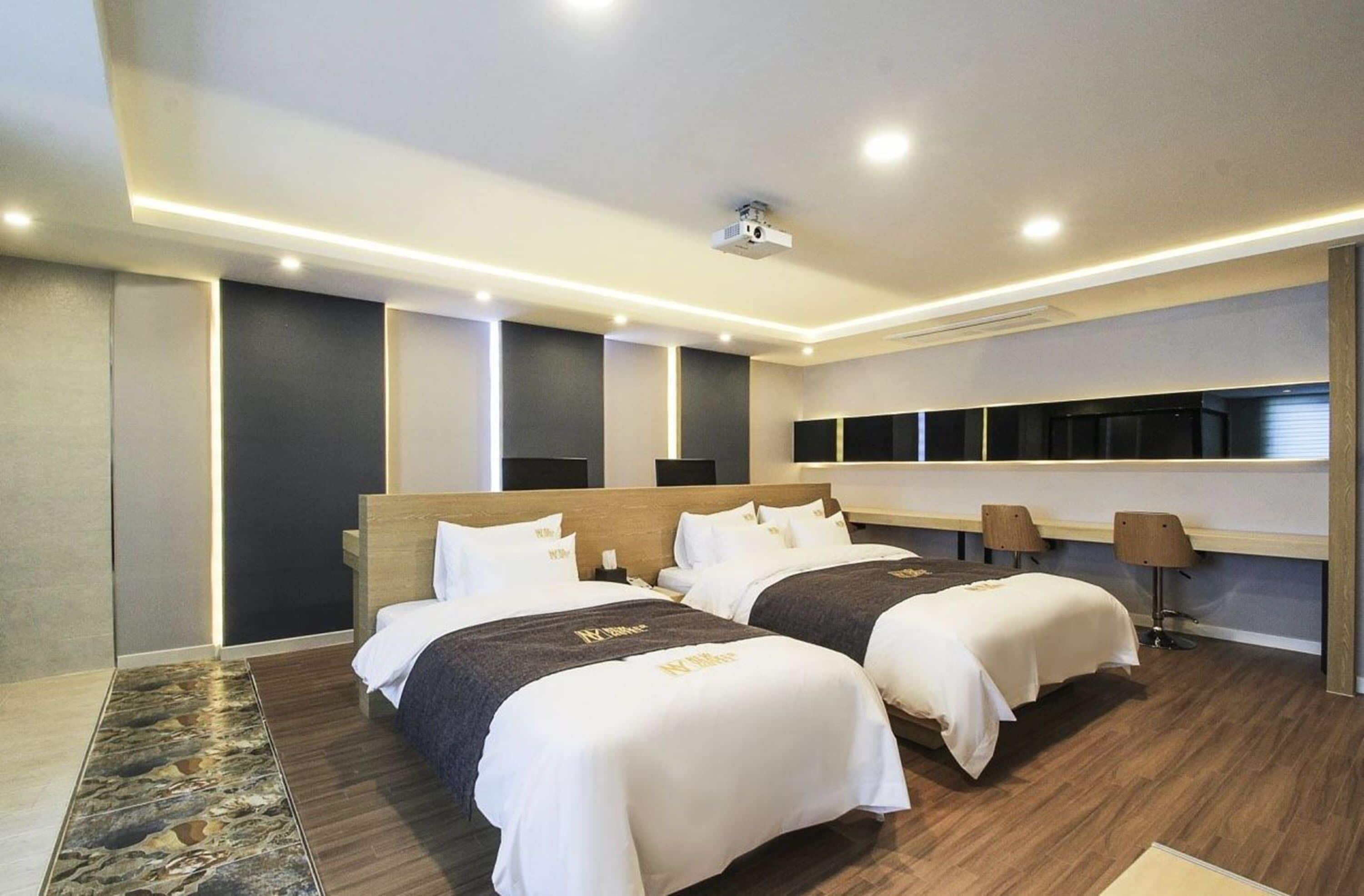 A modern hotel room with two beds, a large mirror, and a seating area with a table and chairs.