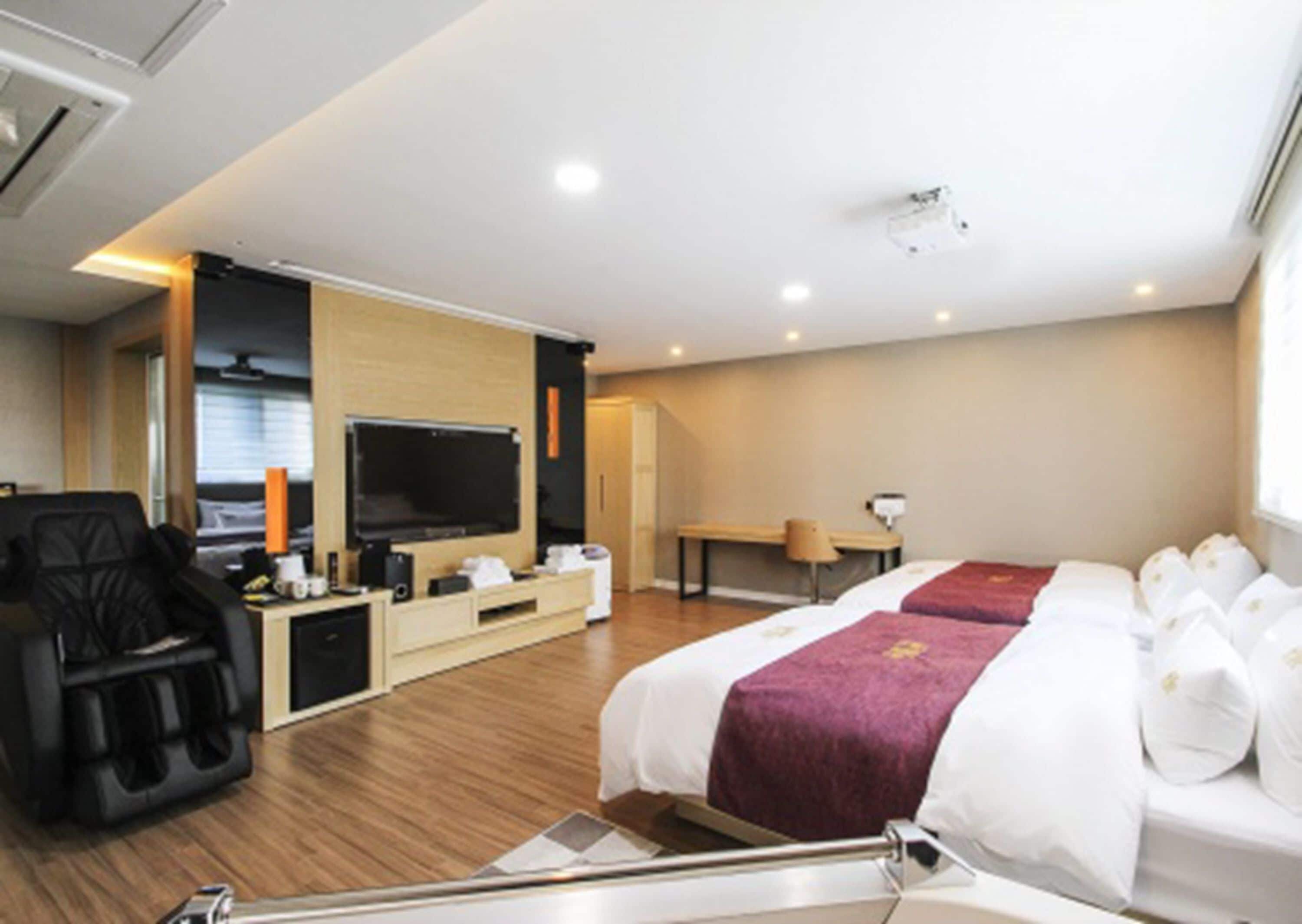 Una habitación de hotel con cama, televisión, escritorio, silla y sillón de masaje.