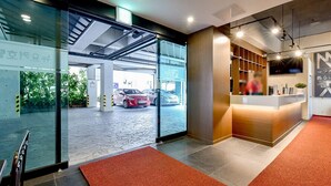 A modern hotel lobby with a reception desk, a glass door leading to a parking garage, and a visible car inside. - New Yorker Hotel (Jinju)