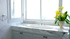Ein Badezimmer mit Marmorwaschbecken, einem Fenster und einer Vase mit gelben Blumen.