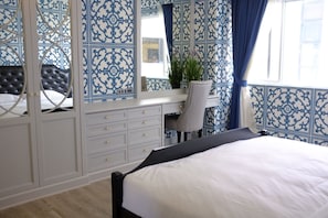A bedroom with a bed, a vanity with a mirror, a chair, and a window with curtains.