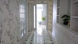 Ein Korridor mit gemustertem Wandpapier, Fliesenboden und einem weißen Schrank mit Schubladen.