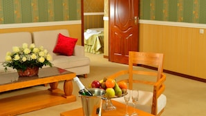 Ein Zimmer mit einem Holztisch, gedeckt mit einer Obstschale, einer Champagnerflasche und zwei Gläsern. Auf dem Tisch steht ein Korbwäscher mit Blumen, daneben ein Holzsessel.