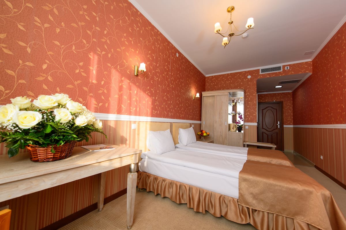 A hotel room with a bed, a desk, and a basket of flowers.