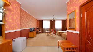 Ein Hotelzimmer mit Essbereich, Fernseher, kleinem Kühlschrank und einer hölzernen Bank.