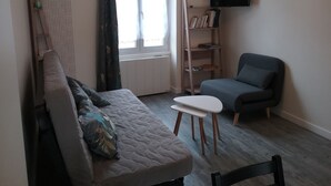Un salon comprenant un canapé, un fauteuil, une petite table, une bibliothèque et un téléviseur fixé au mur.