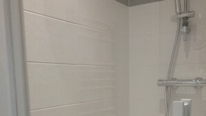 Une douche équipée d’un pommeau de douche à main et d’un panneau de commande fixé au mur.