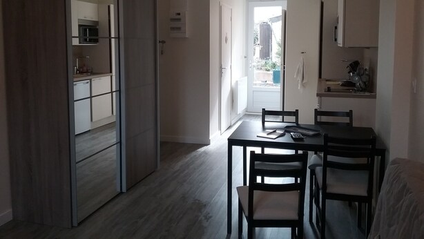 Une cuisine compacte dotée d’appareils électroménagers modernes, un coin repas avec une table et des chaises, et une vue sur un balcon extérieur accessible par une porte ouverte.