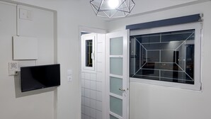 A room with a flat-screen TV mounted on the wall, a window with a geometric pattern, and a door leading to another room. - Nest Studio with Terrace, Acropolis View (Athens)