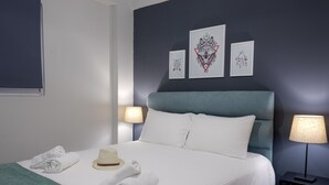 A neatly made bed with white linens, a blue headboard, and a hat on the bed. There are two wall-mounted lamps on either side of the bed. - Nest Studio with Terrace, Acropolis View (Athens)