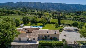 A villa with a tiled roof, a courtyard with a swimming pool, and vineyard fields in the background. - Superb 5 * rated property with spectacular view in Ménerbes (Menerbes)