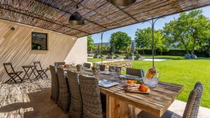 An outdoor dining area with wicker chairs and a wooden table, a pergola overhead, and a view of a well-maintained lawn and trees. - Superb 5 * rated property with spectacular view in Ménerbes (Menerbes)