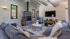 A modern living room with a stone fireplace, a large sofa, and a television mounted on the wall. - Superb 5 * rated property with spectacular view in Ménerbes (Menerbes)