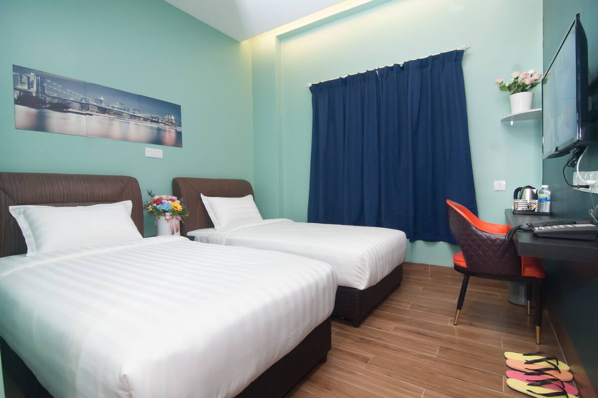 A hotel room with two beds, a desk, a chair, a TV, and a window with curtains.